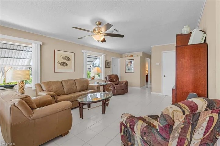 Living area with plenty of natural light, visible vents, a textured ceiling, and a ceiling fan