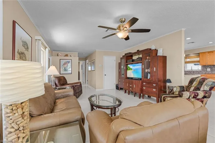 Living area featuring baseboards, ornamental molding, light tile patterned floors, a textured ceiling, and ceiling fan