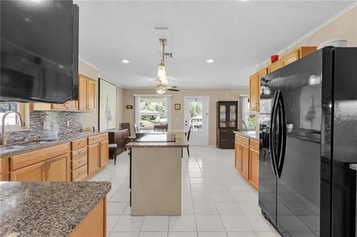 Kitchen featuring black fridge, a sink, a ceiling fan, crown molding, and a kitchen island