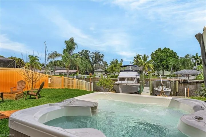 View of pool with a water view, fence, a dock, and a hot tub
