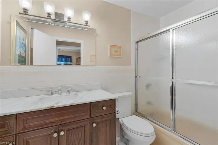 Bathroom featuring toilet, tile walls, combined bath / shower with glass door, and vanity
