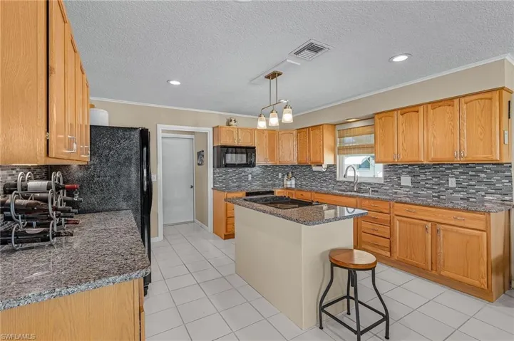 Kitchen featuring dark stone countertops, visible vents, ornamental molding, black appliances, and light tile patterned flooring