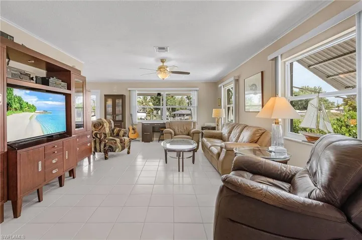 Living room with light tile patterned floors, a ceiling fan, visible vents, and a healthy amount of sunlight
