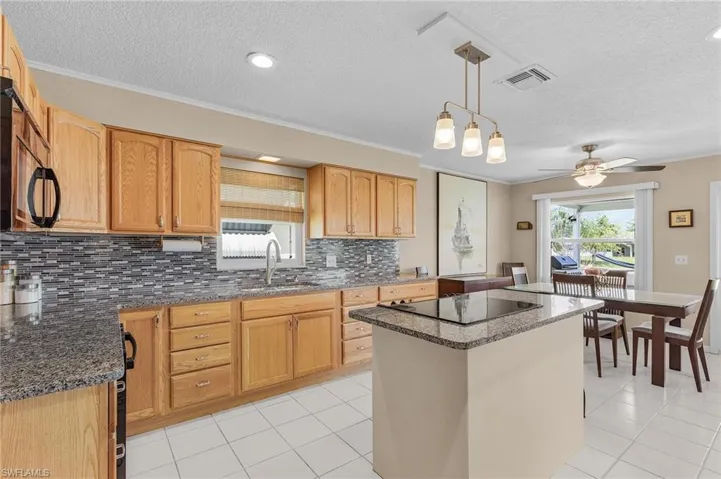 Kitchen featuring visible vents, a sink, ceiling fan, black appliances, and a kitchen island