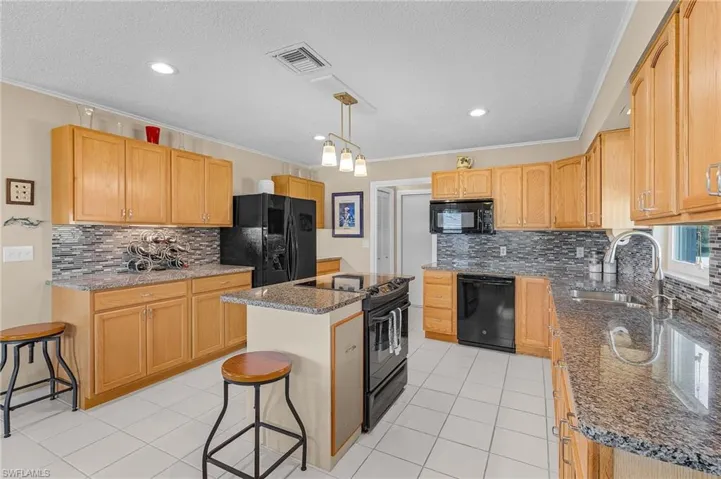 Kitchen with ornamental molding, a center island, black appliances, visible vents, and a sink
