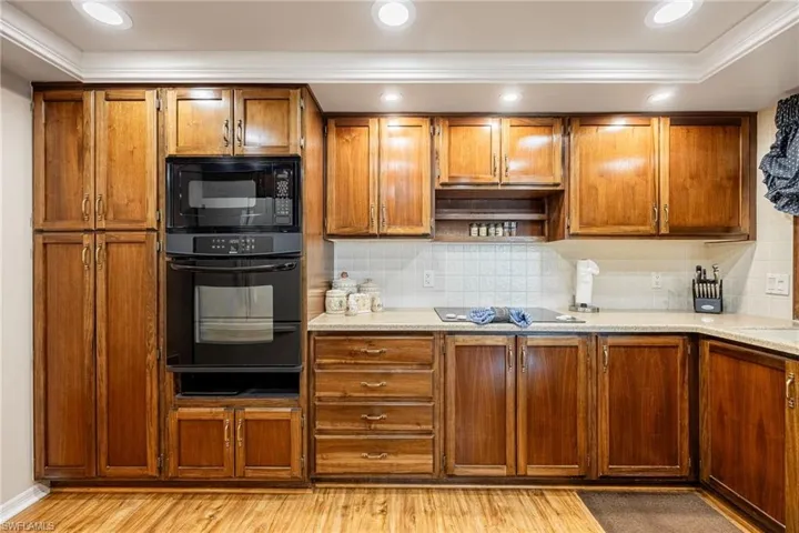 Kitchen with tasteful backsplash, light stone countertops, light hardwood / wood-style flooring, and black appliances
