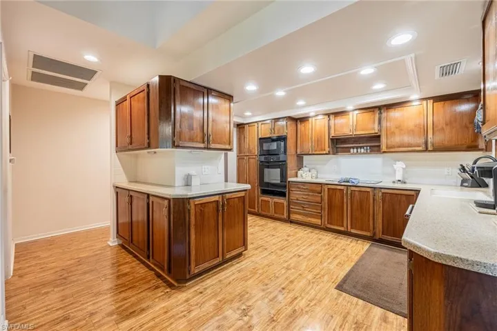 Kitchen featuring sink, tasteful backsplash, a raised ceiling, black appliances, and light wood-type flooring