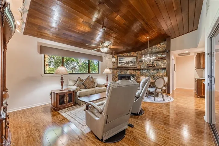 Living room featuring a stone fireplace, wood ceiling, light hardwood / wood-style flooring, and vaulted ceiling