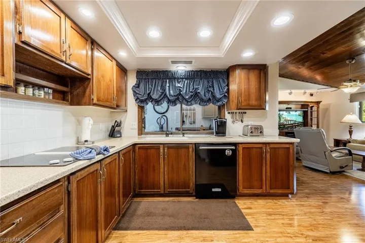 Kitchen with sink, ornamental molding, light wood-type flooring, black dishwasher, and a tray ceiling