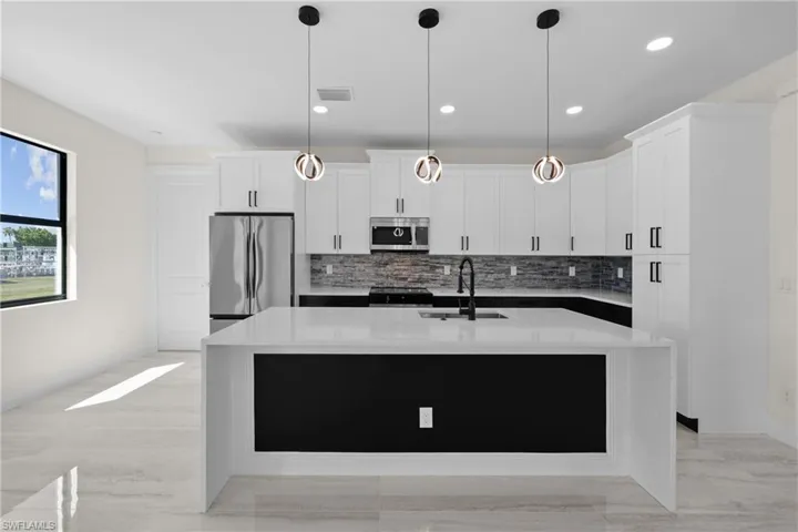 Kitchen with a sink, decorative light fixtures, appliances with stainless steel finishes, white cabinets, and a kitchen island with sink