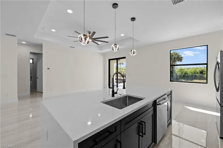 Kitchen with an island with sink, a sink, a tray ceiling, dishwasher, and ceiling fan