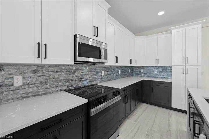 Kitchen with dark cabinetry, light stone countertops, range with electric stovetop, white cabinetry, and stainless steel microwave