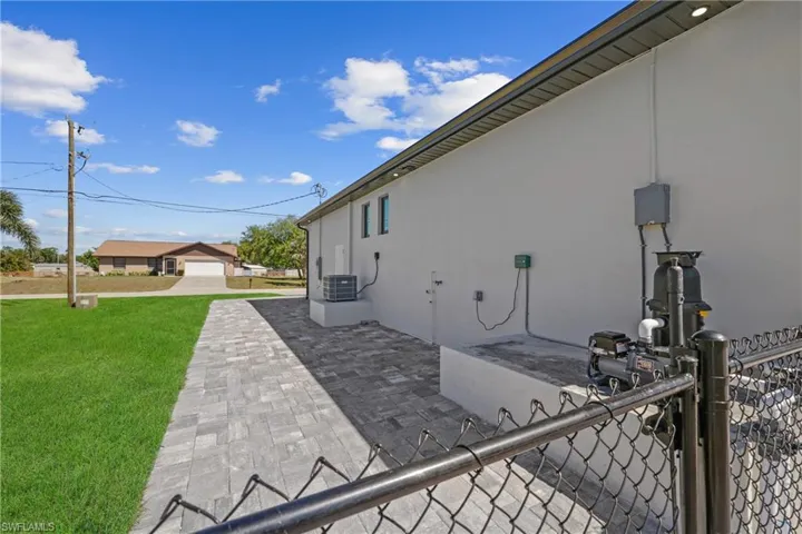 View of side of property featuring central air condition unit, fence, a lawn, and stucco siding