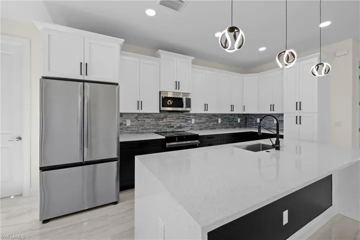 Kitchen with visible vents, a kitchen island with sink, a sink, stainless steel appliances, and white cabinets