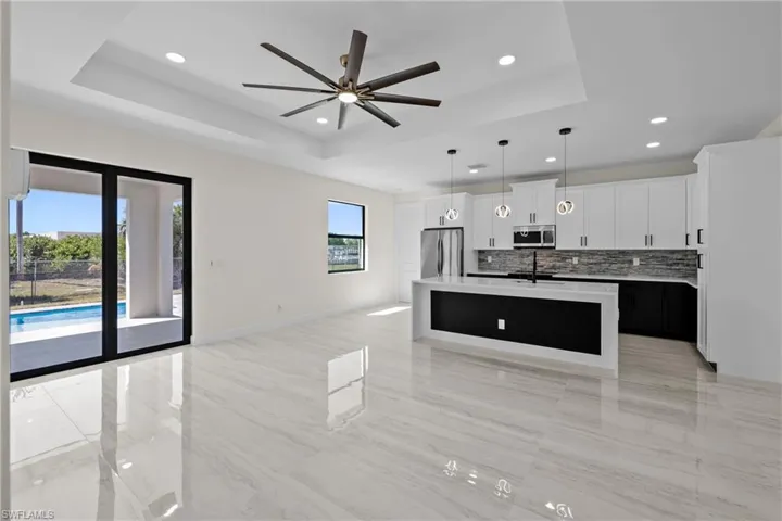 Kitchen featuring tasteful backsplash, ceiling fan, open floor plan, a tray ceiling, and appliances with stainless steel finishes