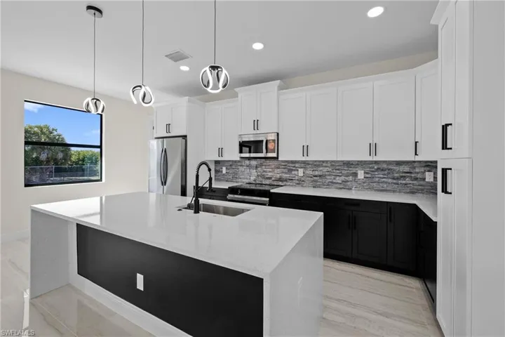 Kitchen featuring visible vents, a kitchen island with sink, a sink, backsplash, and stainless steel appliances
