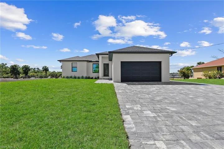 Prairie-style home featuring stucco siding, an attached garage, decorative driveway, and a front yard