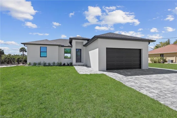 Prairie-style house featuring a front yard, decorative driveway, an attached garage, and stucco siding
