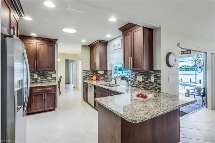 Kitchen with light stone counters, light tile flooring, backsplash, appliances with stainless steel finishes, and sink