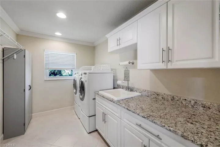 Clothes washing area featuring cabinets, washer and clothes dryer, crown molding, sink, and light tile floors