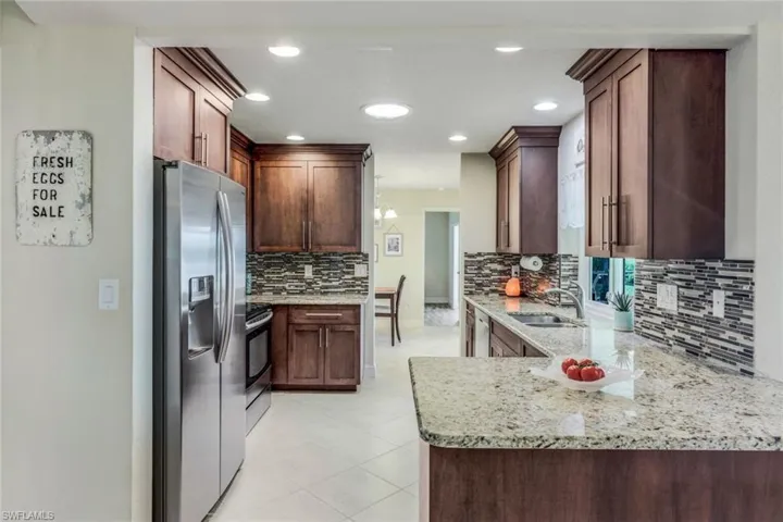 Kitchen featuring light stone countertops, stainless steel appliances, kitchen peninsula, sink, and tasteful backsplash