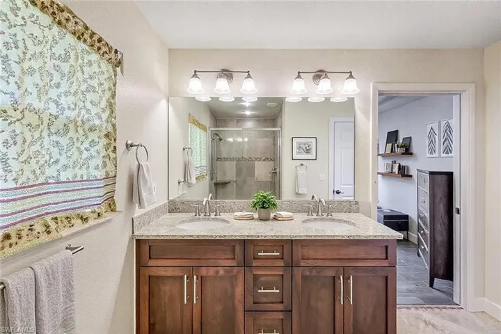 Full bathroom featuring a sink, baseboards, double vanity, and a shower stall