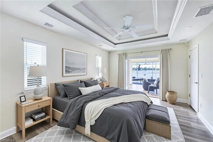 Bedroom with a tray ceiling, wood finished floors, and visible vents