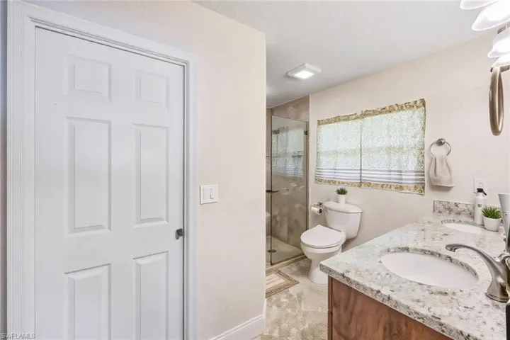 Bathroom featuring double vanity, toilet, a stall shower, and a sink