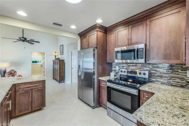 Kitchen featuring light stone countertops, ceiling fan, stainless steel appliances, backsplash, and light tile floors
