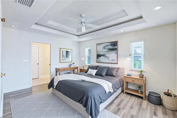 Bedroom with visible vents, wood finished floors, baseboards, a raised ceiling, and ceiling fan