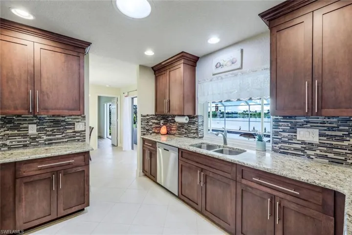 Kitchen with tasteful backsplash, light stone countertops, stainless steel dishwasher, sink, and light tile floors