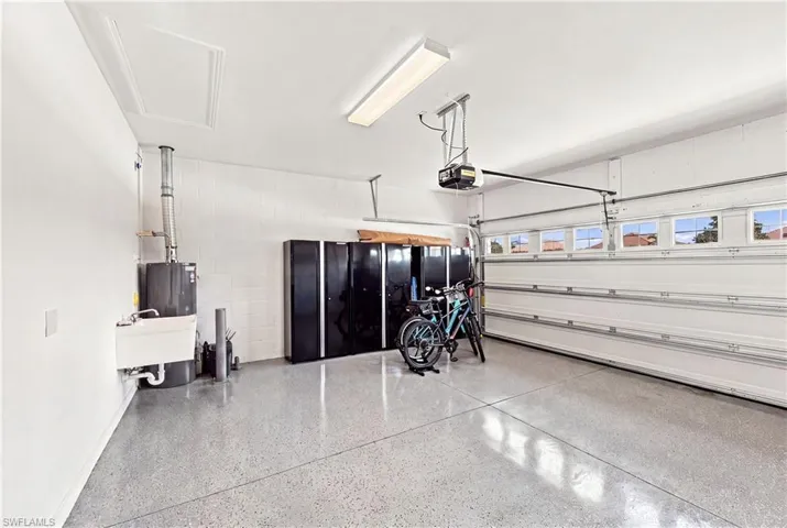 Epoxy-coated flooring, built-in utility sink, garage door with upper windows, automatic garage door opener, and ceiling-mounted fluorescent lighting