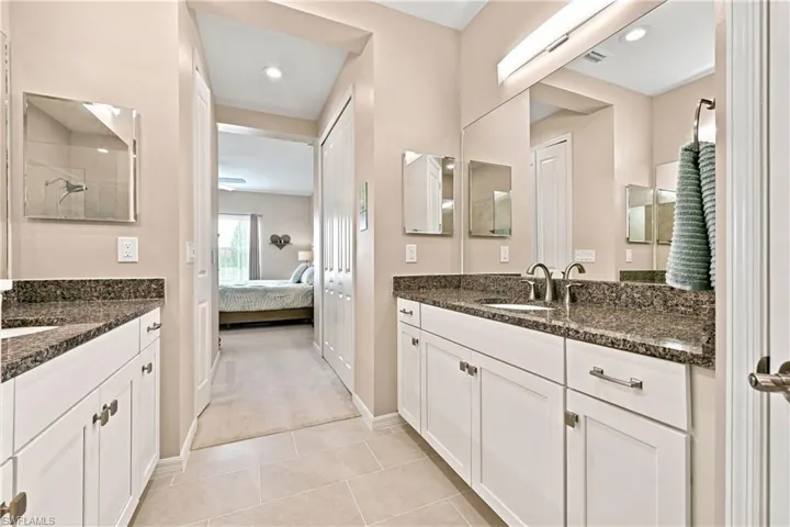 Dual vanity with white cabinetry, granite countertops, and polished chrome hardware