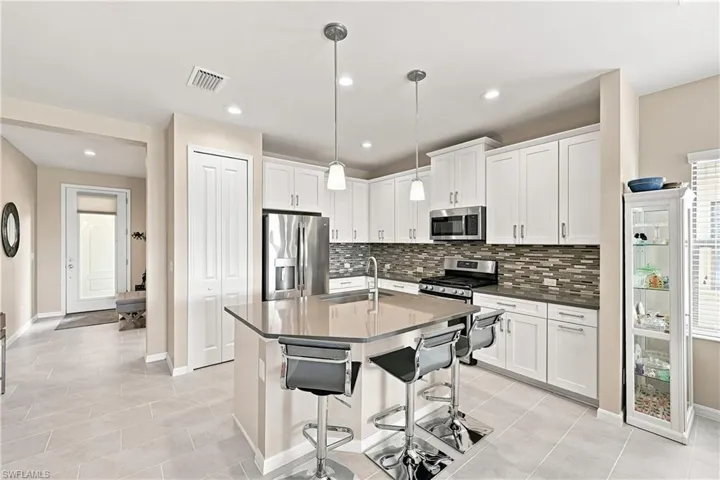 Kitchen featuring stainless steel appliances, a center island with seating, pendant lighting, shaker-style cabinetry, and a tile backsplash