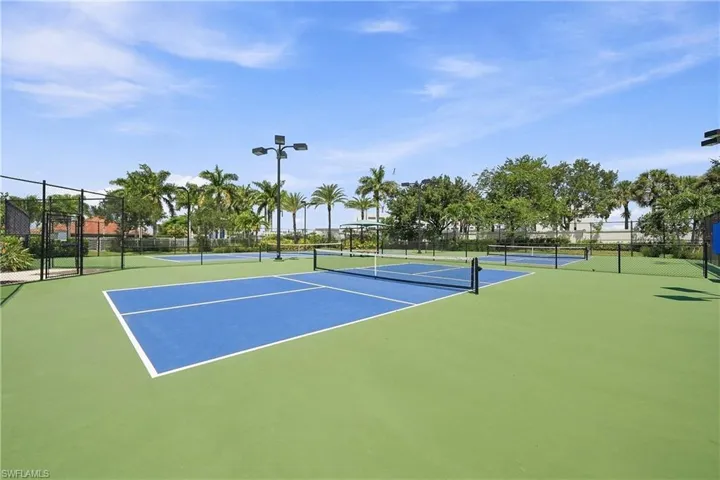 Multiple outdoor courts with green and blue surfaces, black perimeter fencing, and overhead lighting fixtures
