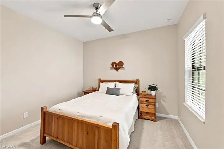 Neutral-toned walls with carpeted flooring, featuring a ceiling fan with integrated lighting and a window with blinds