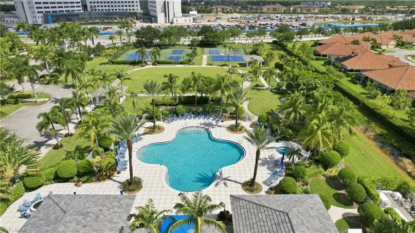 Clover-shaped swimming pool with a surrounding paved deck, multiple tennis courts, and manicured green spaces