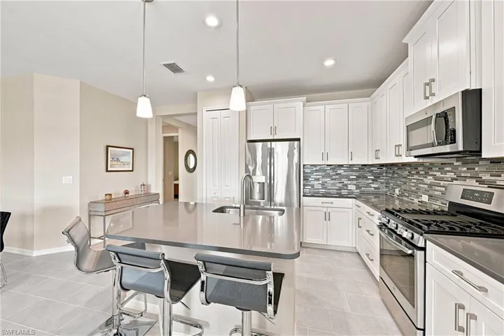 Kitchen featuring a large island with sink, white shaker-style cabinetry, mosaic tile backsplash, stainless steel appliances, and recessed lighting