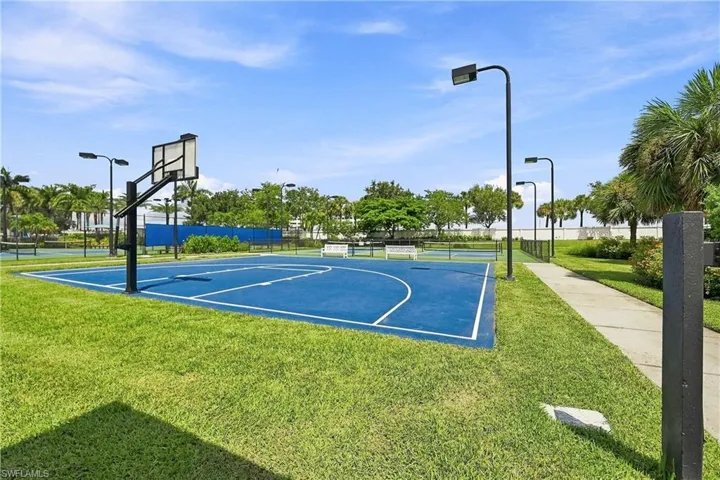 Basketball court featuring a blue playing surface, perimeter fencing, and integrated lighting