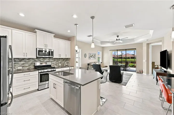 Open-concept living space featuring a kitchen with stainless steel appliances, white cabinetry, and a center island with a sink