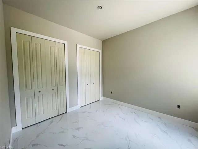 Unfurnished bedroom with multiple closets, light marble finish flooring, and baseboards