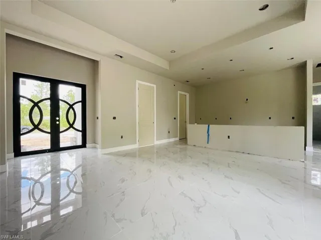 Empty room with a tray ceiling, french doors, baseboards, recessed lighting, and light marble finish floors
