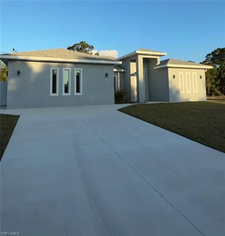 View of front of house with concrete driveway, stucco siding, a front yard, and a shingled roof