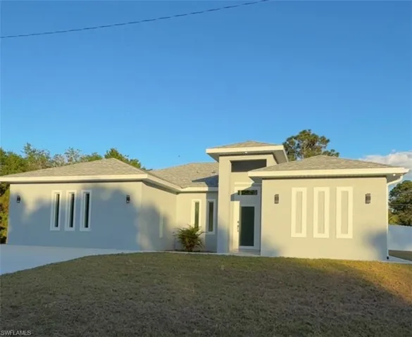 Front of the house with stucco siding, a front yard, roof with shingles, and driveway