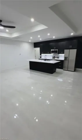 Kitchen featuring dark cabinets, a center island with sink, light countertops, stainless steel appliances, and recessed lighting