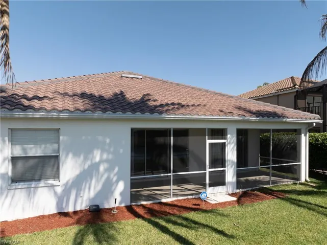 Rear view of property with a tiled roof, a lawn, stucco siding, and a sunroom