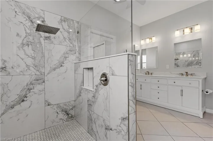 Bathroom featuring double vanity, a marble finish shower, ceiling fan, and light tile patterned floors