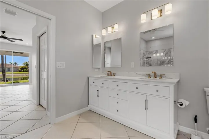 Bathroom featuring a ceiling fan, double vanity, a marble finish shower, and light tile patterned floors