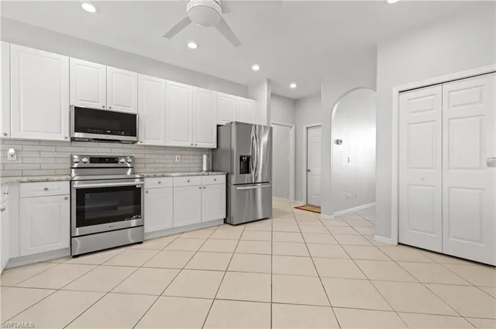 Kitchen with arched walkways, stainless steel appliances, a ceiling fan, white cabinetry, and light stone counters