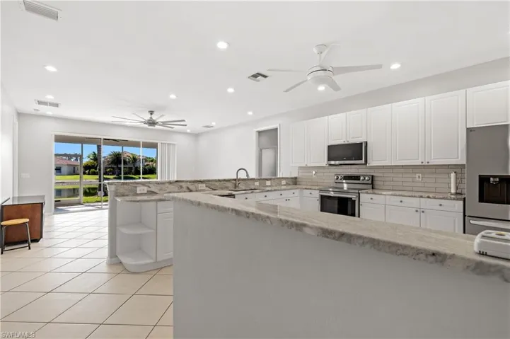 Kitchen with white cabinetry, stainless steel appliances, a peninsula, ceiling fan, and decorative backsplash